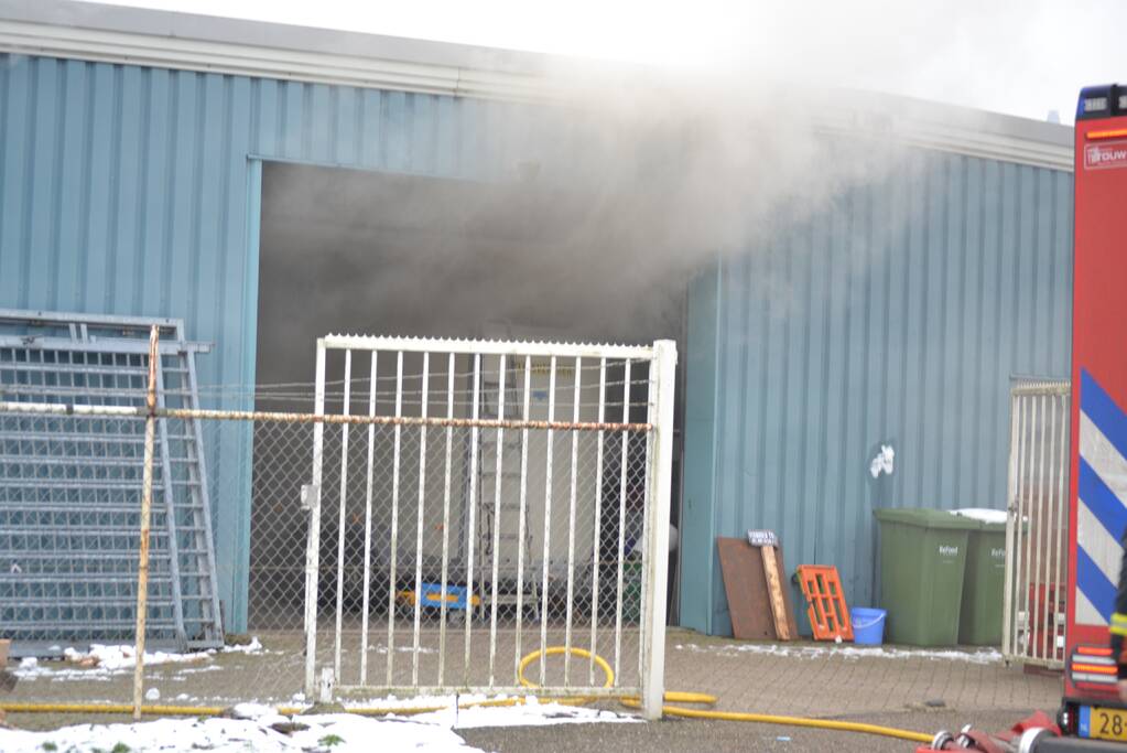 Houtopslag tegen loods aan vat vlam