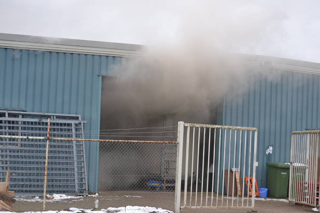 Houtopslag tegen loods aan vat vlam