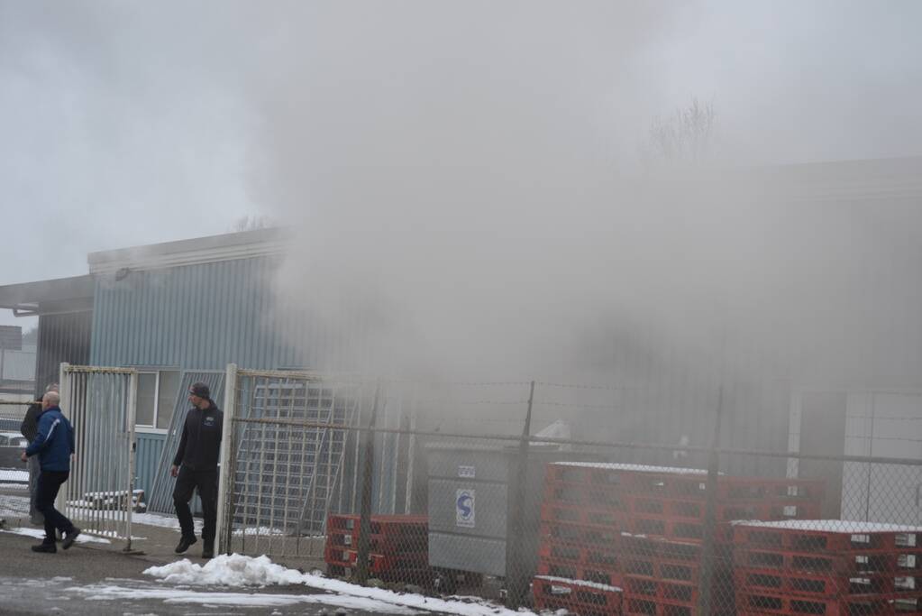 Houtopslag tegen loods aan vat vlam