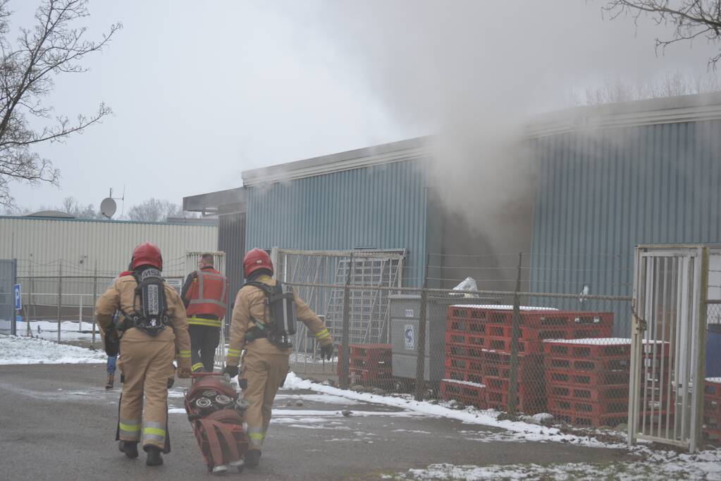 Houtopslag tegen loods aan vat vlam