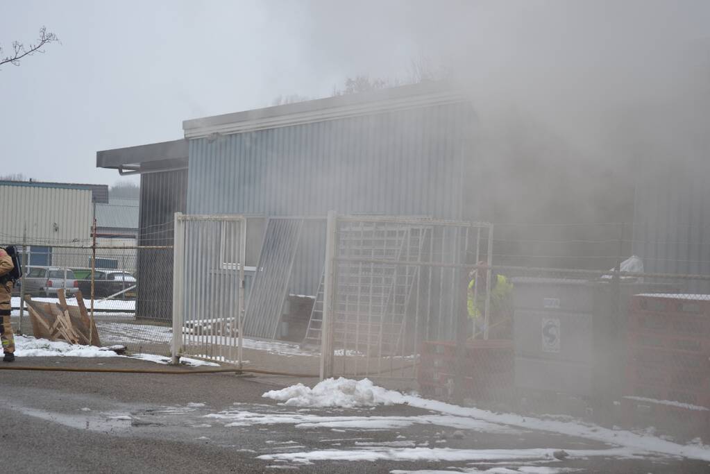 Houtopslag tegen loods aan vat vlam