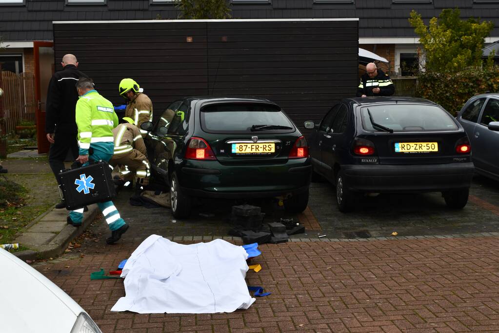 Persoon bekneld onder auto