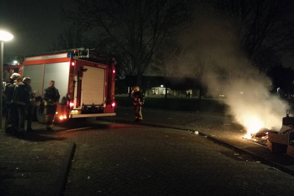 Vuurwerkresten in de brand naast papiercontainer