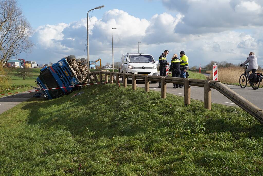 Vrachtwagen met zand van dijk gekanteld