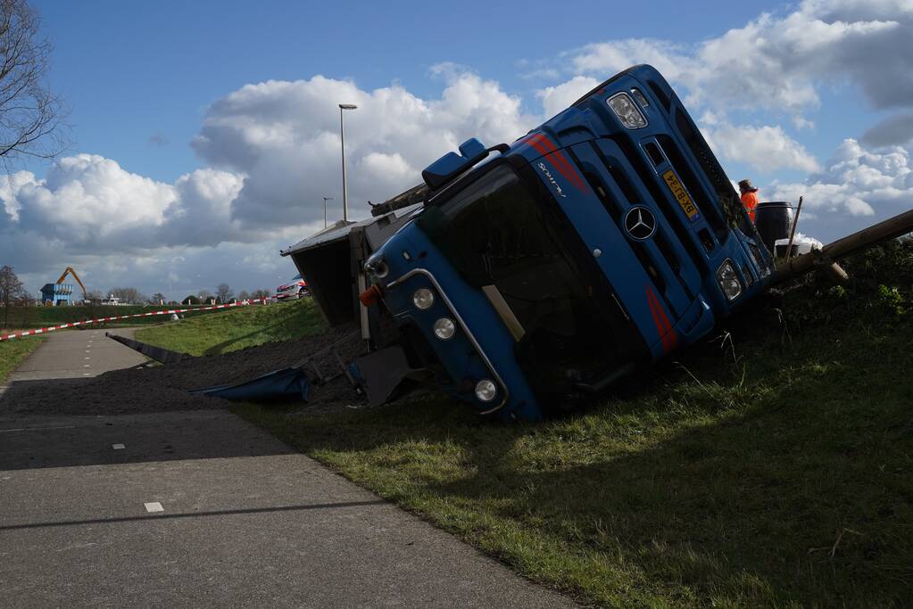 Vrachtwagen met zand van dijk gekanteld
