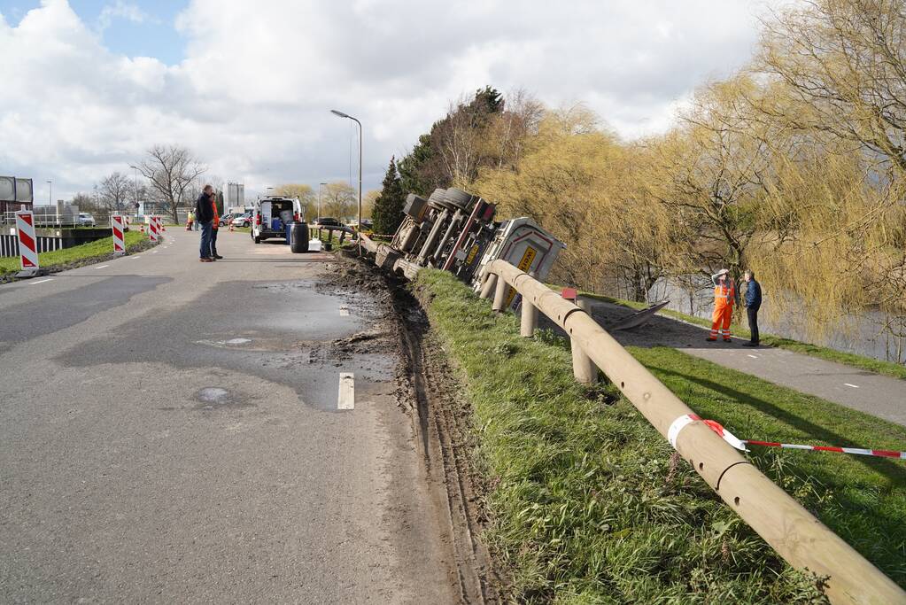 Vrachtwagen met zand van dijk gekanteld