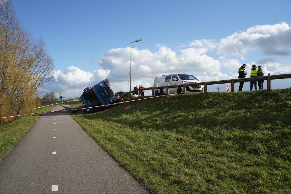 Vrachtwagen met zand van dijk gekanteld