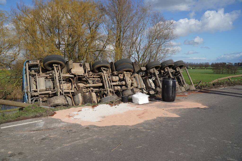 Vrachtwagen met zand van dijk gekanteld