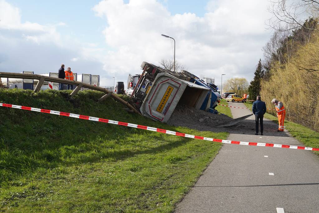 Vrachtwagen met zand van dijk gekanteld