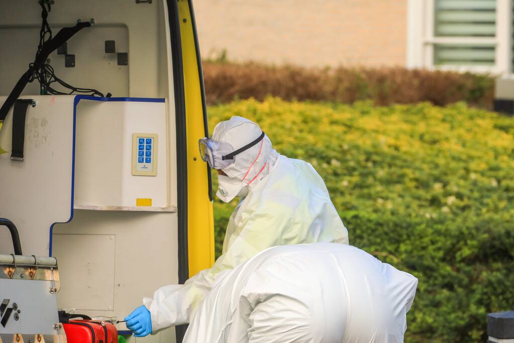 Mannen in witte pakken halen vermoedelijke coronapatiënt uit huis