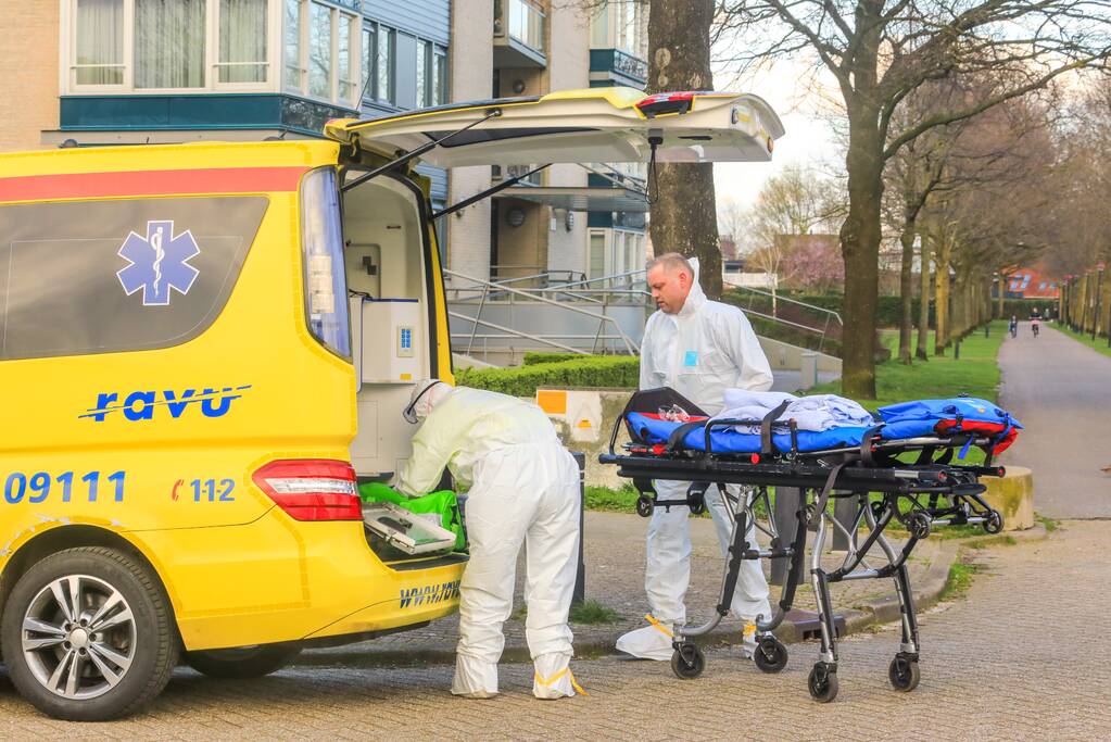 Mannen in witte pakken halen vermoedelijke coronapatiënt uit huis