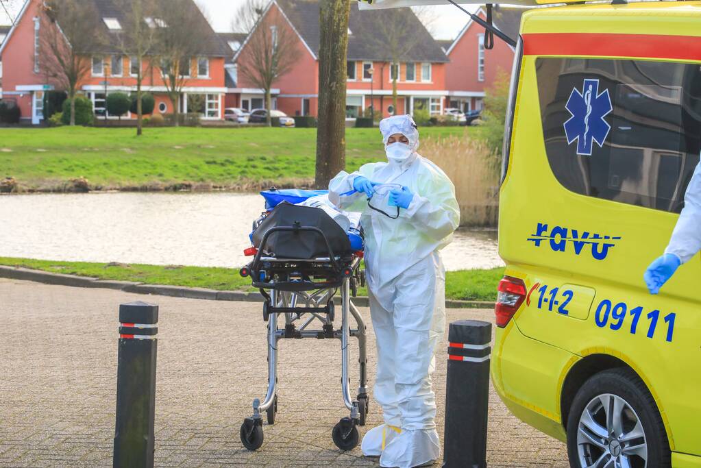 Mannen in witte pakken halen vermoedelijke coronapatiënt uit huis