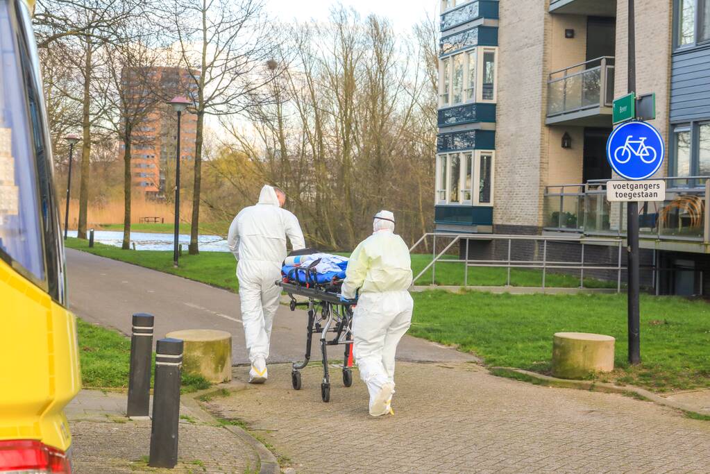 Mannen in witte pakken halen vermoedelijke coronapatiënt uit huis