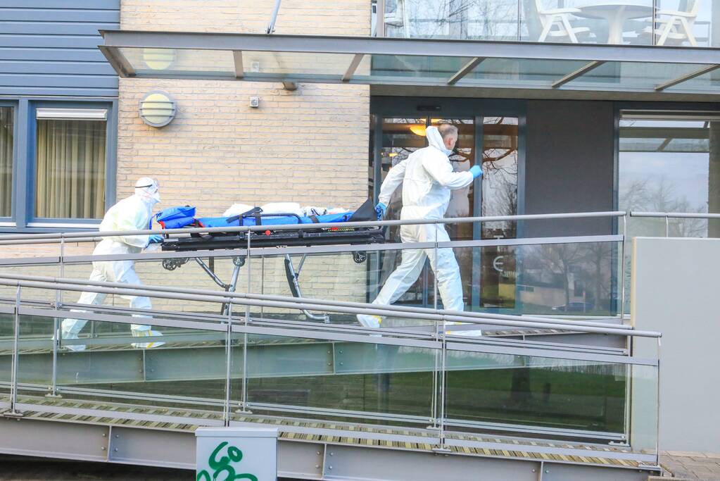 Mannen in witte pakken halen vermoedelijke coronapatiënt uit huis