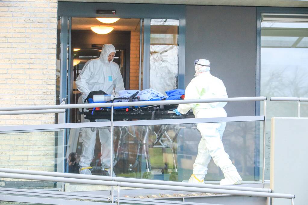Mannen in witte pakken halen vermoedelijke coronapatiënt uit huis