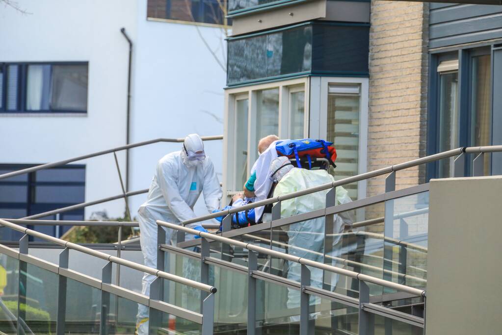 Mannen in witte pakken halen vermoedelijke coronapatiënt uit huis