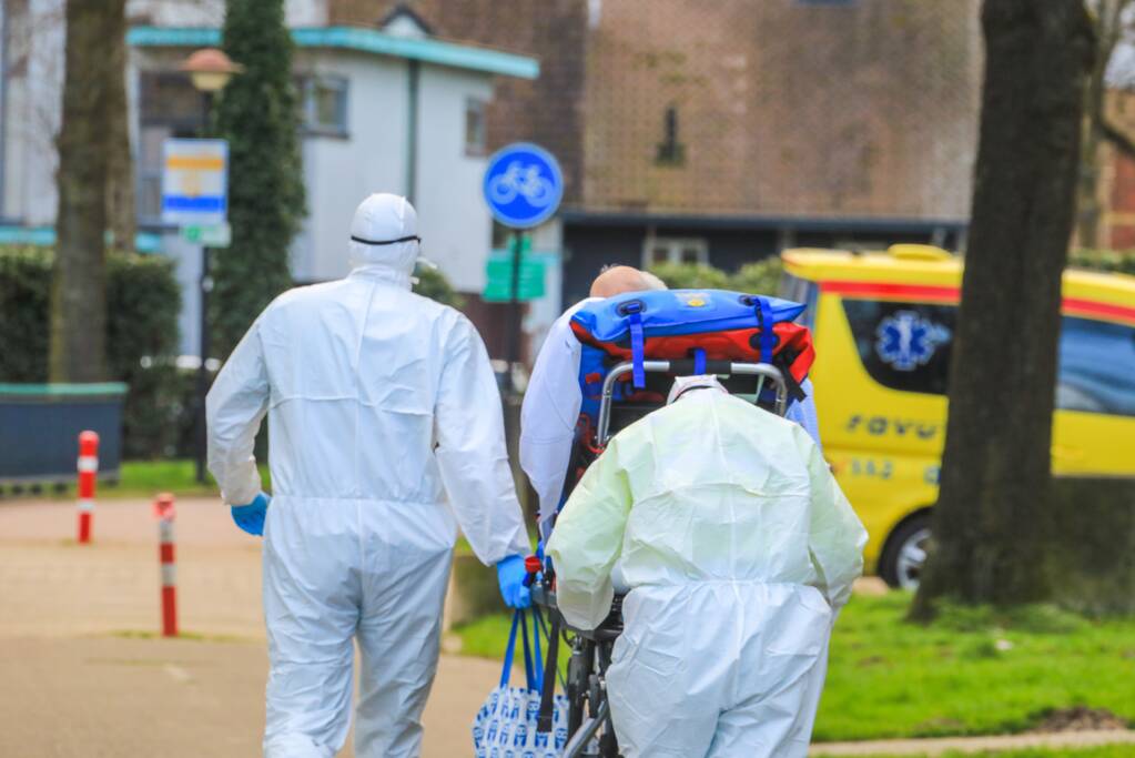Mannen in witte pakken halen vermoedelijke coronapatiënt uit huis