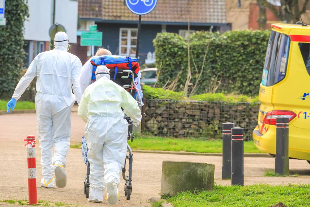 Mannen in witte pakken halen vermoedelijke coronapatiënt uit huis