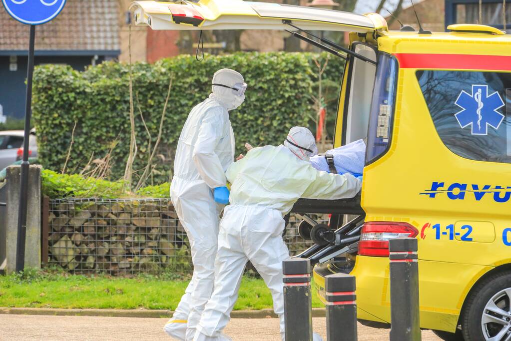 Mannen in witte pakken halen vermoedelijke coronapatiënt uit huis