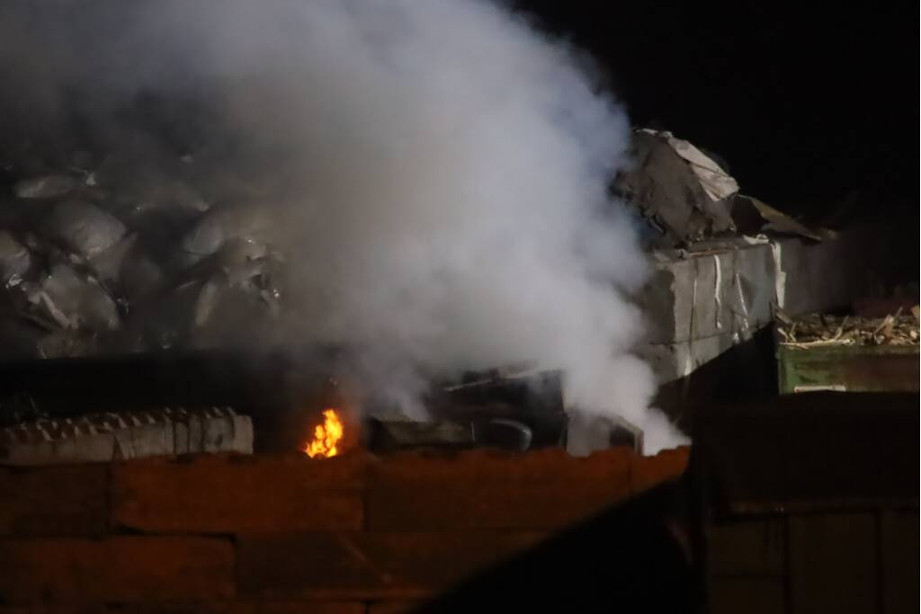 Grote berg afvalhout in brand naast houtopslag