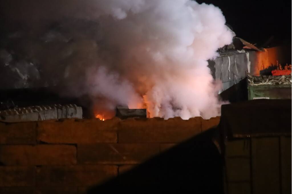 Grote berg afvalhout in brand naast houtopslag