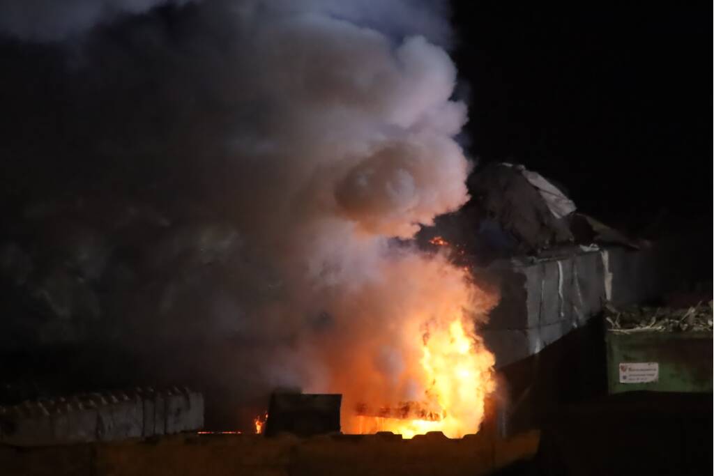 Grote berg afvalhout in brand naast houtopslag