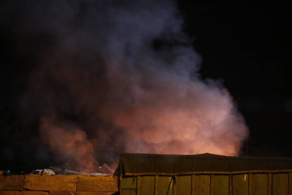 Grote berg afvalhout in brand naast houtopslag