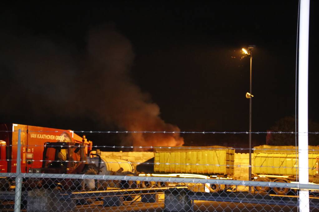 Grote berg afvalhout in brand naast houtopslag