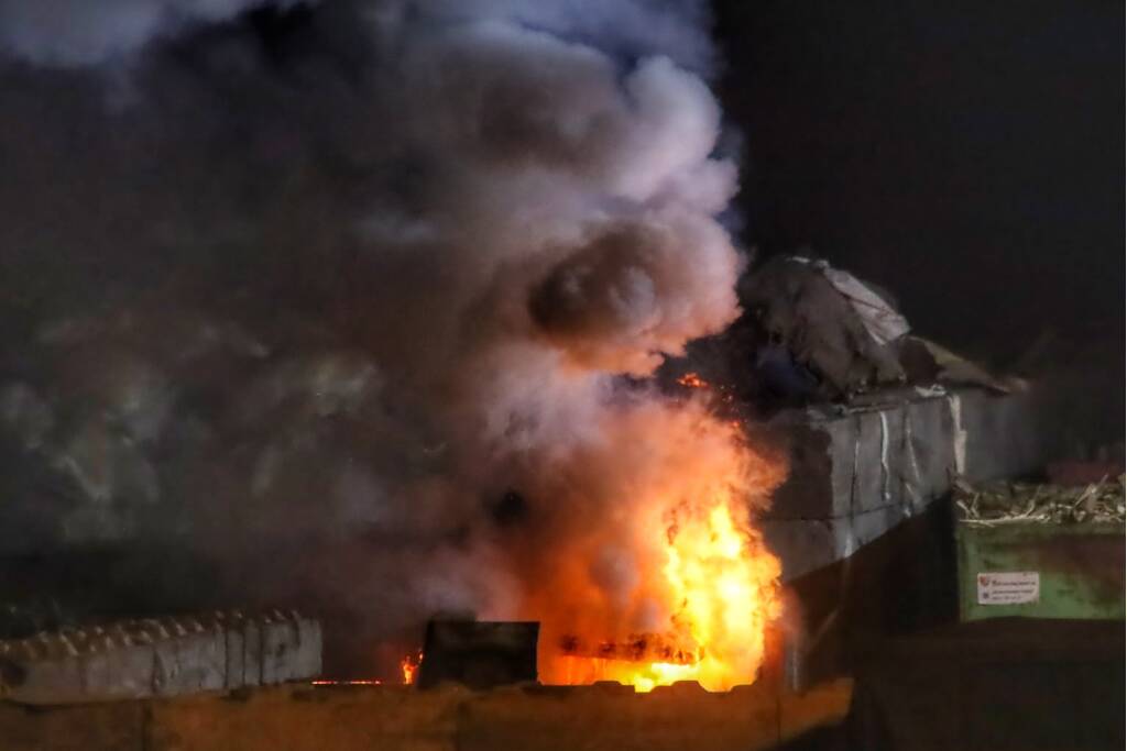 Grote berg afvalhout in brand naast houtopslag