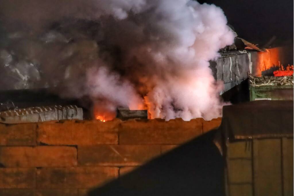 Grote berg afvalhout in brand naast houtopslag