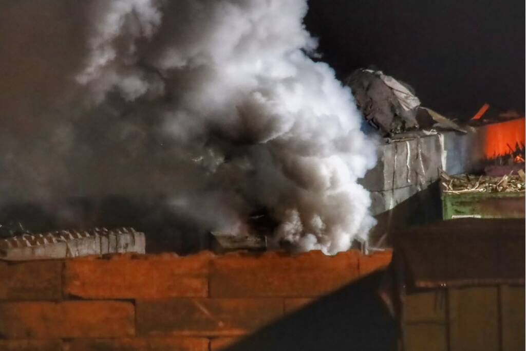 Grote berg afvalhout in brand naast houtopslag