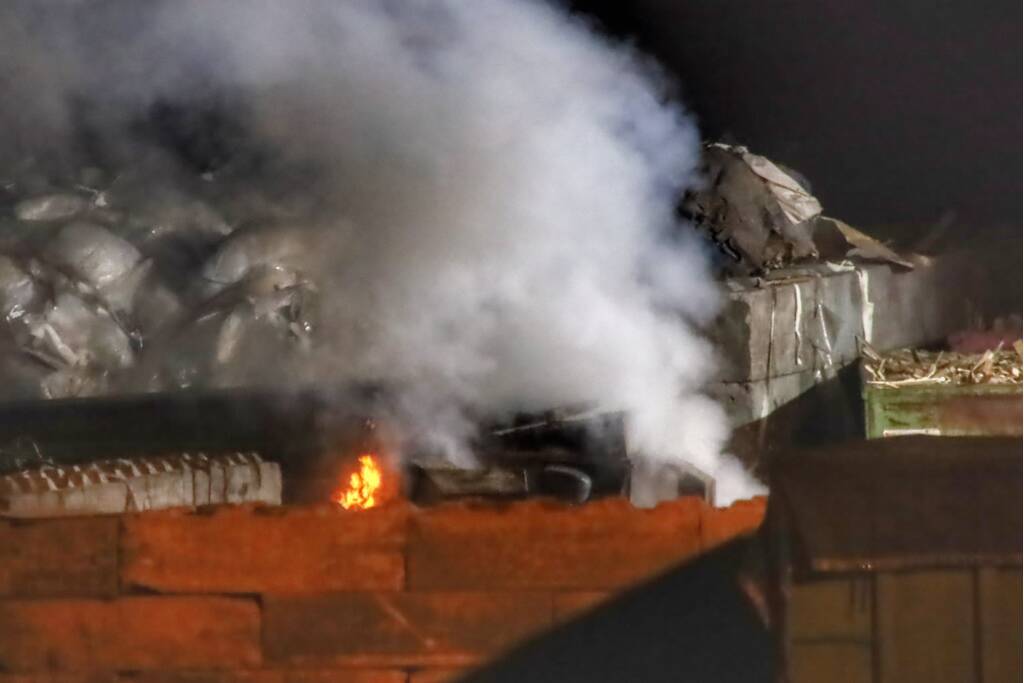 Grote berg afvalhout in brand naast houtopslag