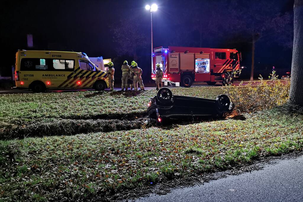 Personenauto ligt op zijn kop in berm