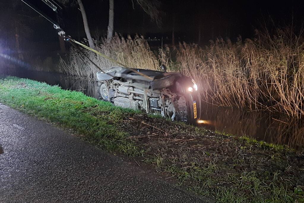 Auto vliegt uit de bocht en belandt op zijn kant in sloot
