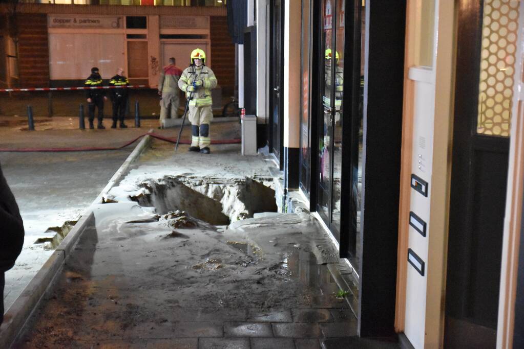 Kelders vol water na sinkhole in trottoir