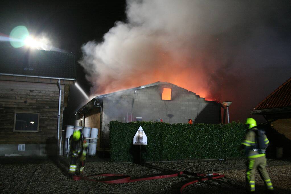 Grote uitslaande brand in loods achter woning