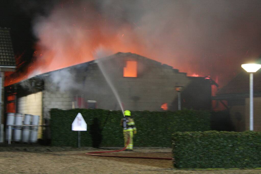 Grote uitslaande brand in loods achter woning