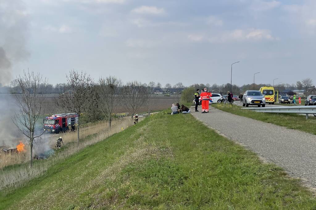 Auto glijdt van dijk af na botsing en vliegt in brand