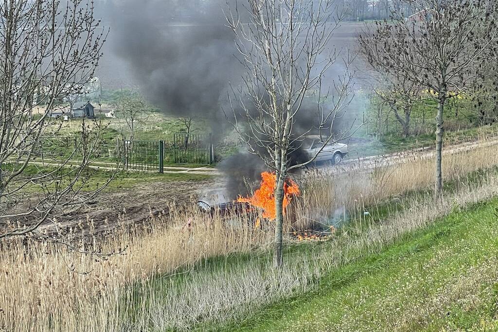 Auto glijdt van dijk af na botsing en vliegt in brand