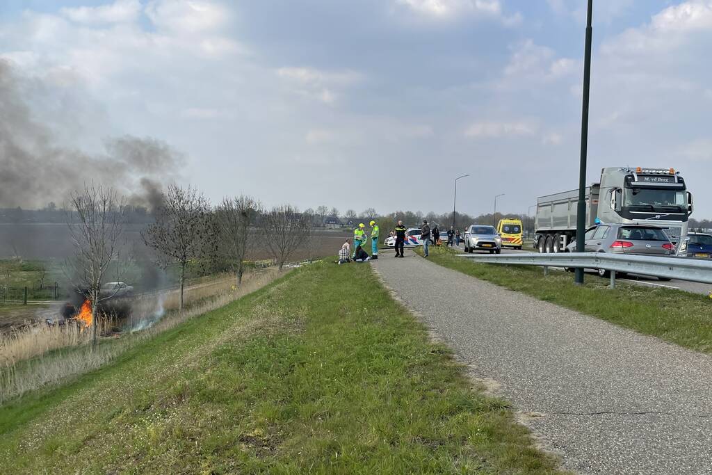 Auto glijdt van dijk af na botsing en vliegt in brand