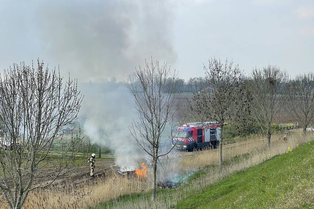 Auto glijdt van dijk af na botsing en vliegt in brand