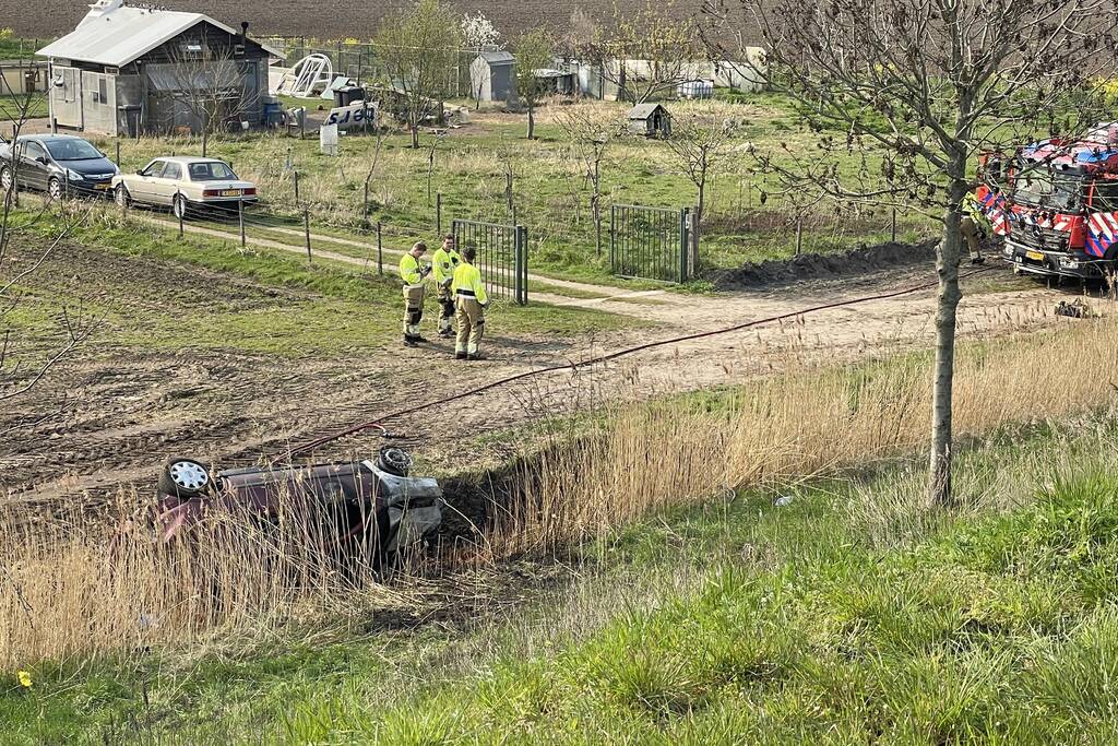 Auto glijdt van dijk af na botsing en vliegt in brand