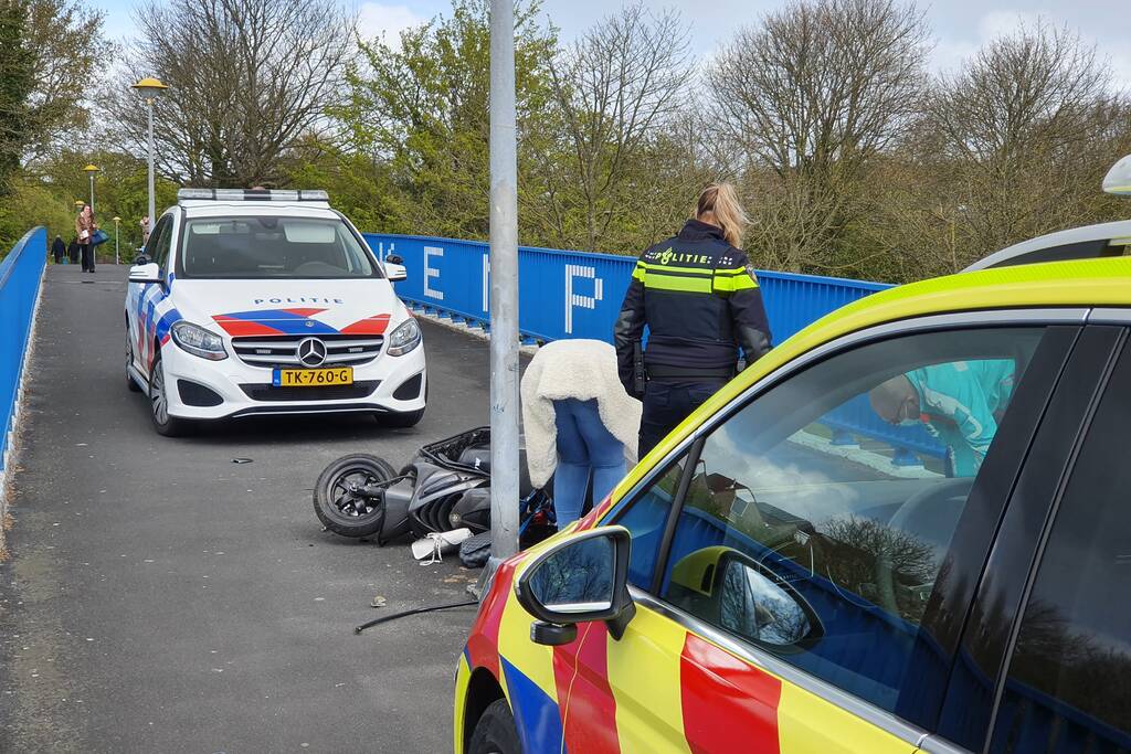 Man en vrouw gaan met scooter onderuit op fietsbrug