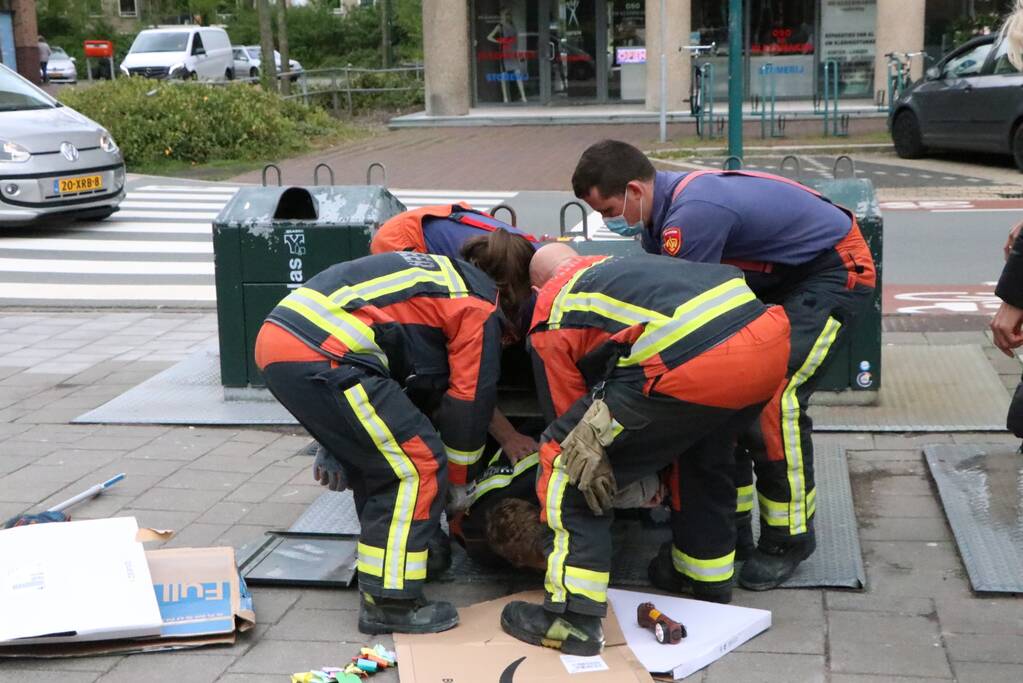 Brandweerman kruipt in ondergrondse papiercontainer voor verloren horloge