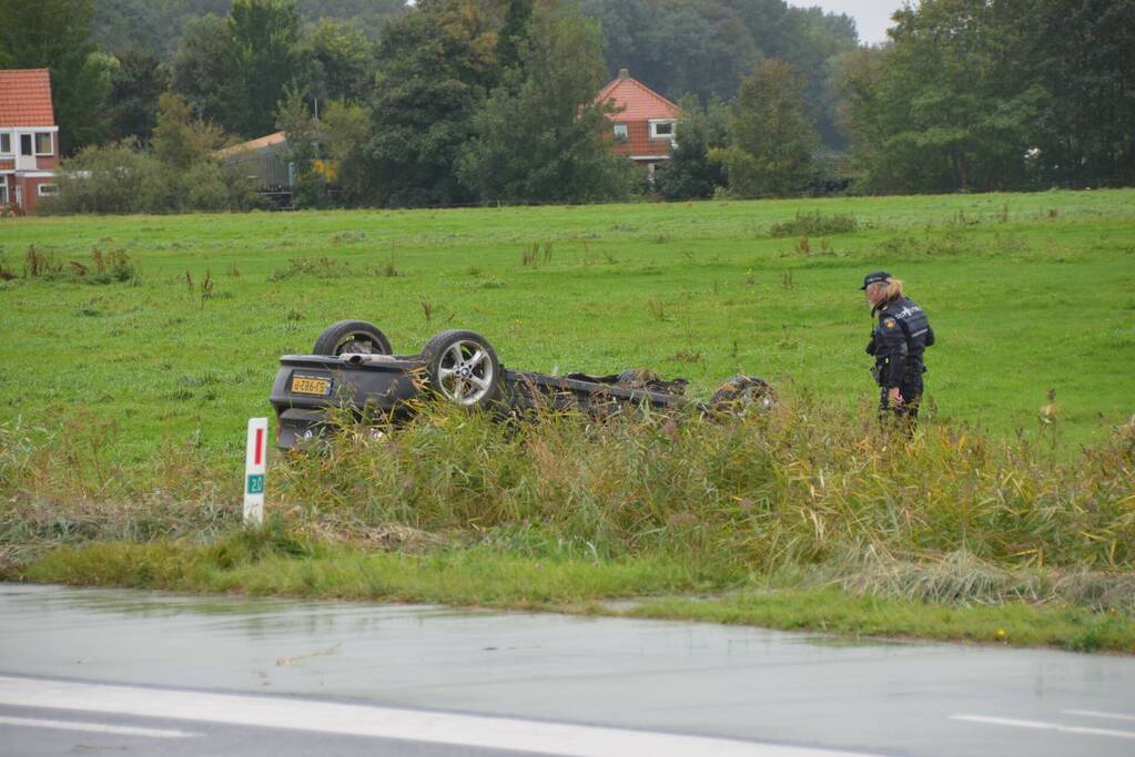 Auto raakt na botsing van de weg en belandt op de kop in weiland