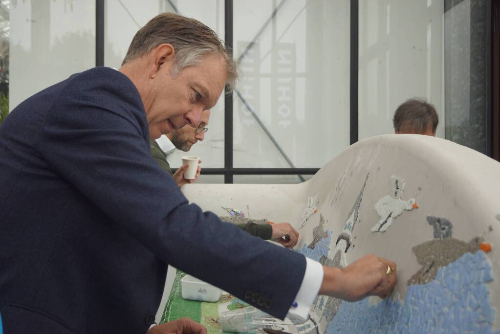 Burgemeester Röell helpt bij beplakken Social Sofa bij woonwarenhuis Nijhof