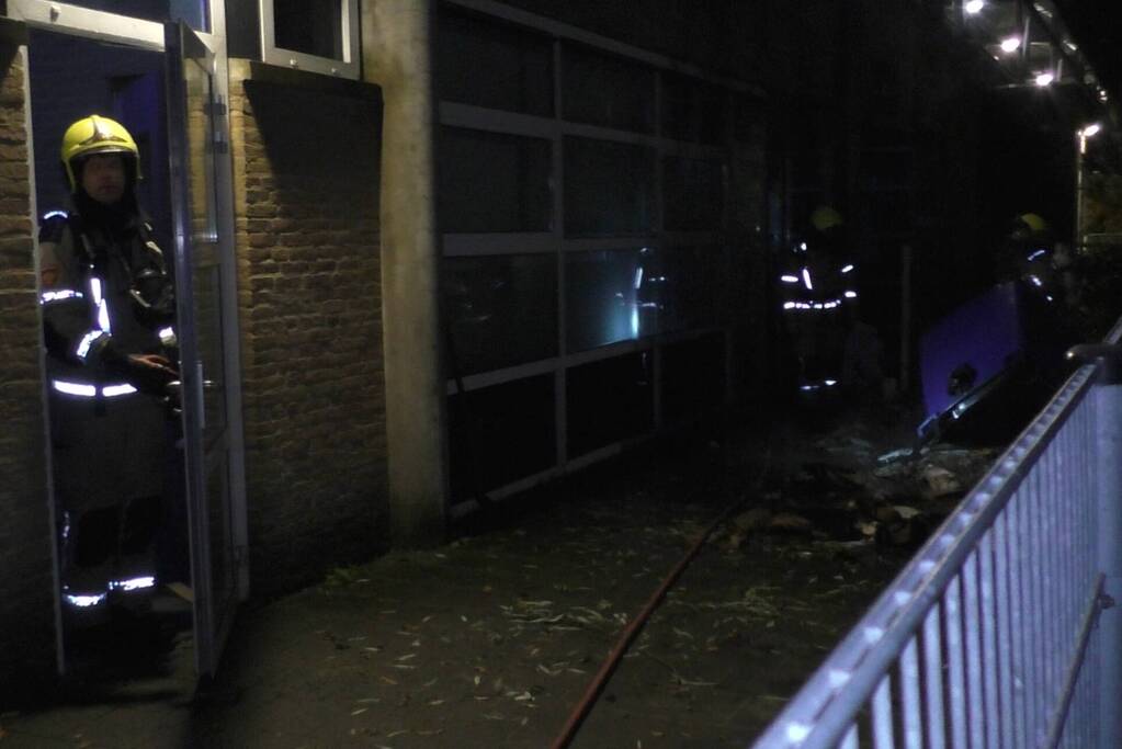 Brandweer blust brandende container tegen school