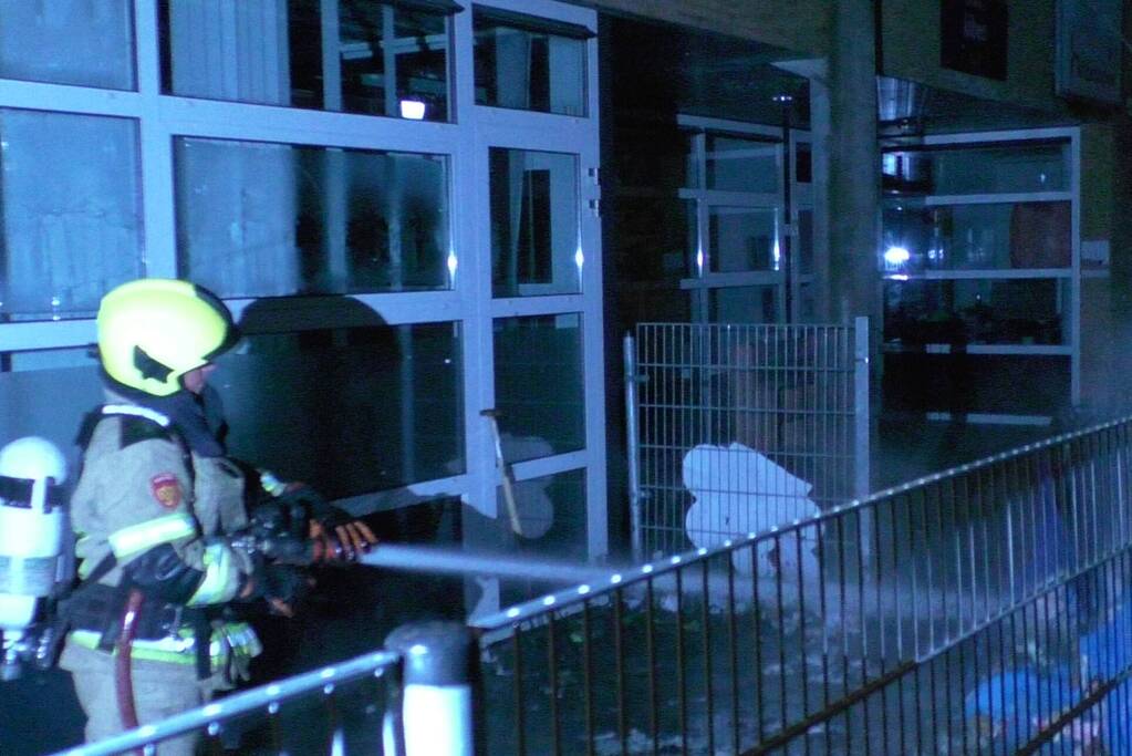 Brandweer blust brandende container tegen school