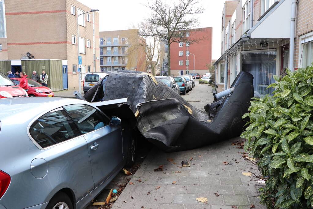 Dakbedekking van flat waait over auto's en lantaarnpalen
