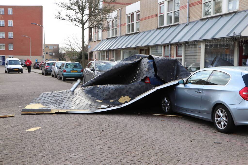 Dakbedekking van flat waait over auto's en lantaarnpalen